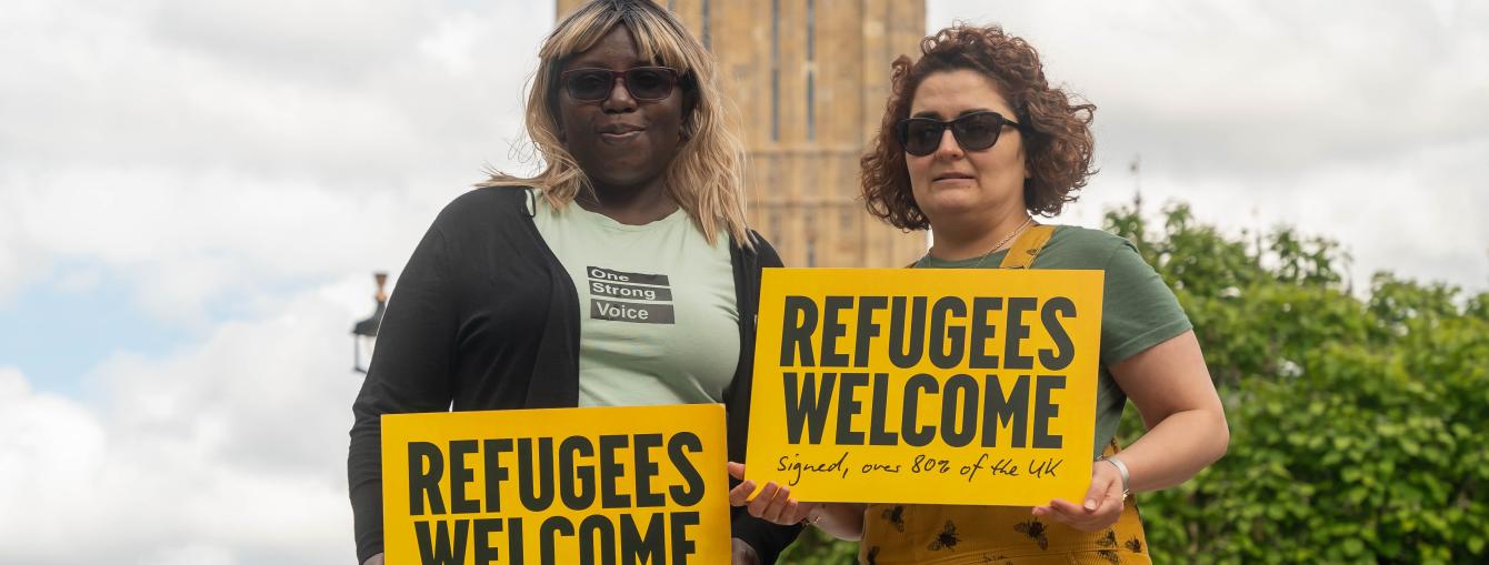 Two women holding a 'Refugees Welcome' sign outside Parliament