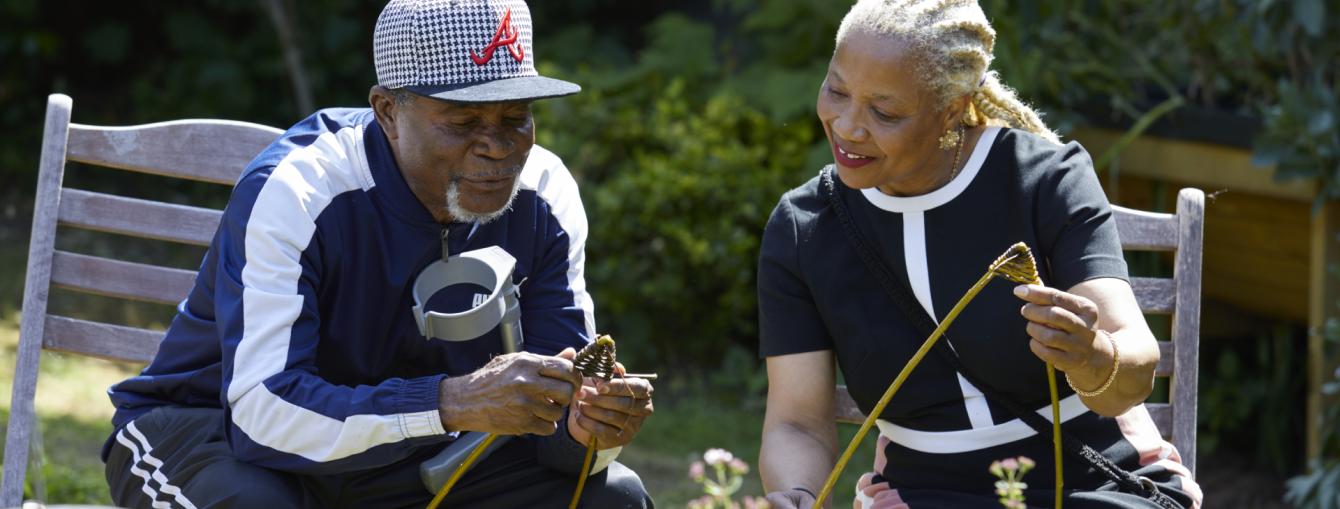 A man and a woman smile as they learn weaving in a sunny garden