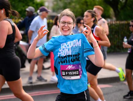 woman with glasses in a freedom from torture tee running whilst smiling at camera