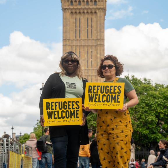 Two women holding a 'Refugees Welcome' sign outside Parliament