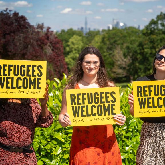 Three women holding a 'Refugees welcome' placard smiling at camera