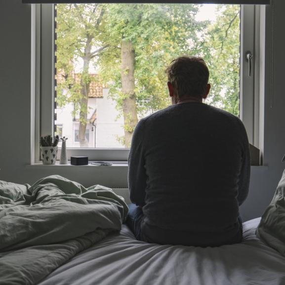 Rear view of an unrecognisable mature man sitting on his bed looking out of the window