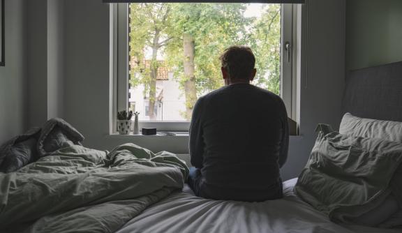 Rear view of an unrecognisable mature man sitting on his bed looking out of the window